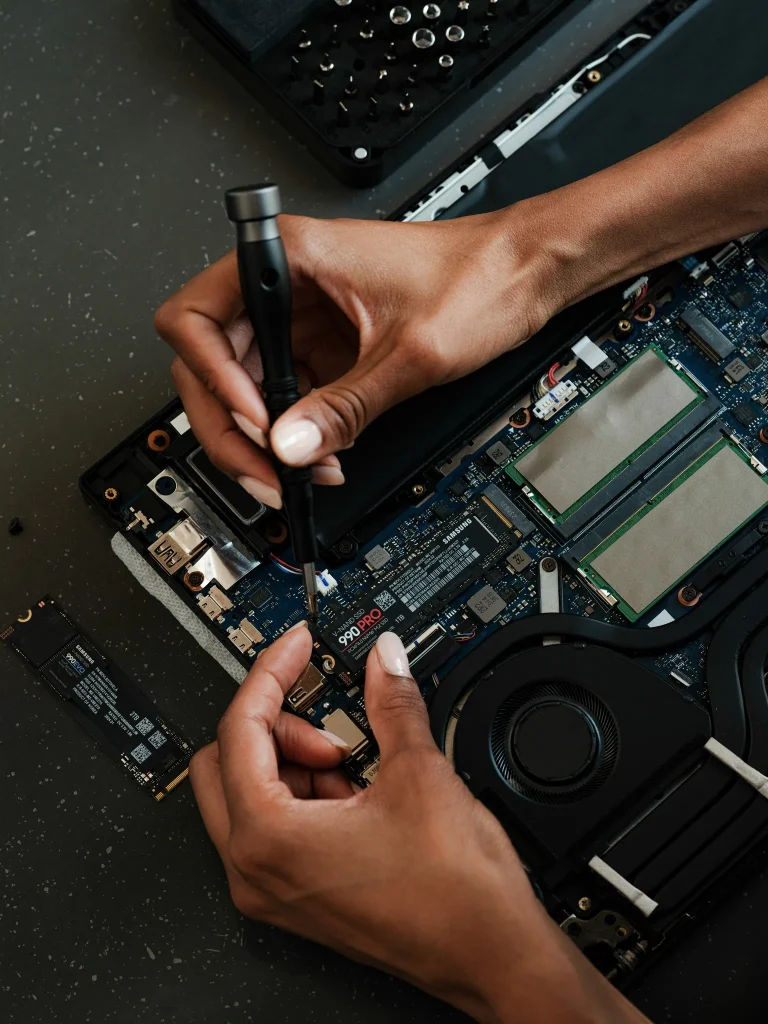 Hands repairing a laptop motherboard.